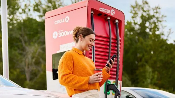 Bild av en kvinna som tittar på mobilen medan hon laddar bilen