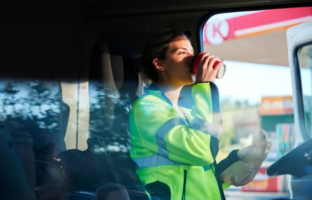 Woman getting into her truck drinking coffee and holding a sandwich